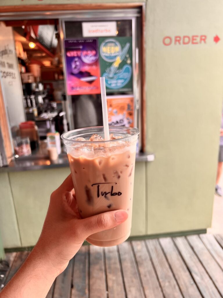 a hand holding an iced coffee in front of a coffee shop