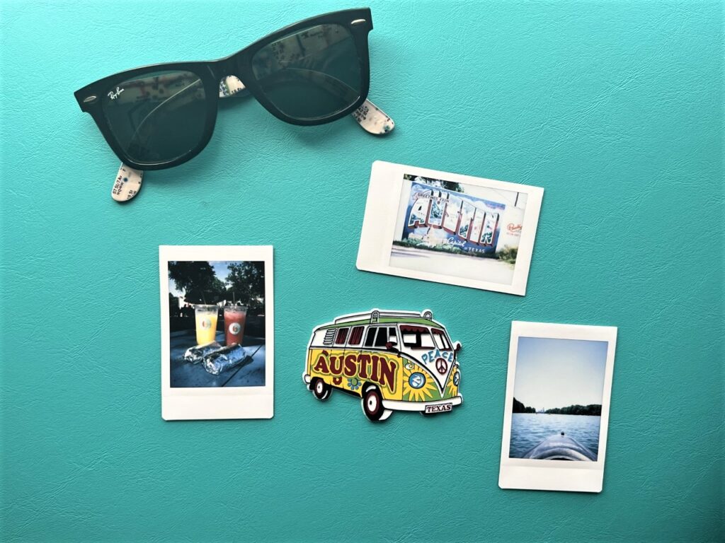 A Flatlay of Polaroid images of Austin Texas, an Austin hippie van magnet, and a pair of ray-ban sunglasses