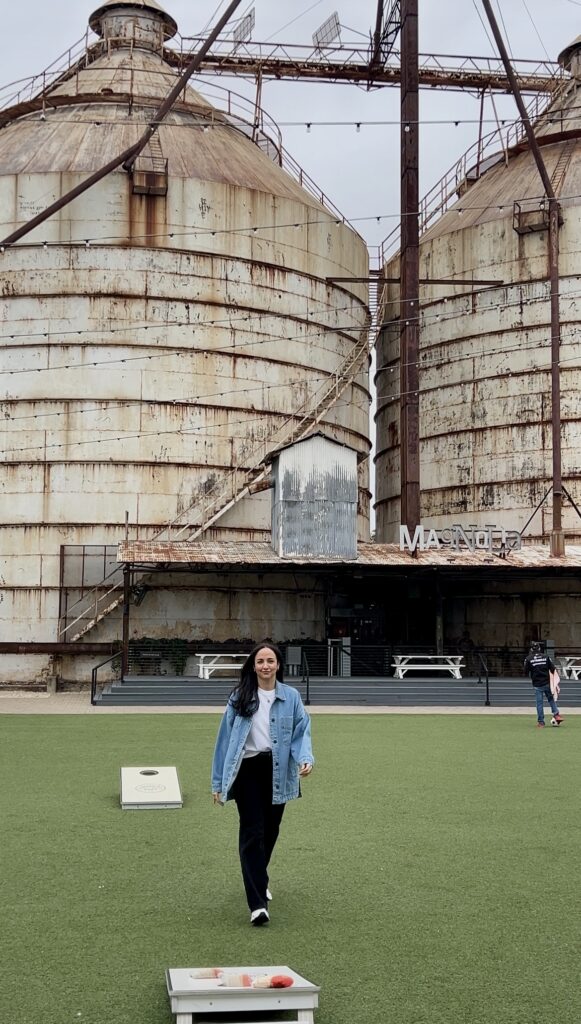 a woman standing on a lawn with two large silos behind her