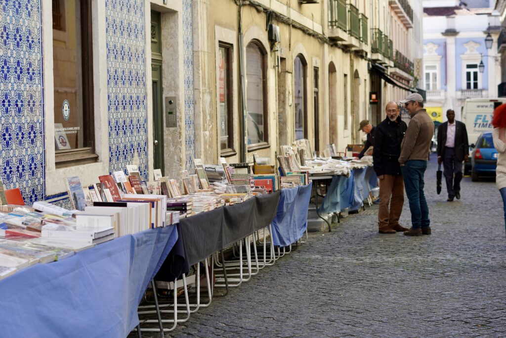 tables with books outside of a bookstore and people shopping and looking at books