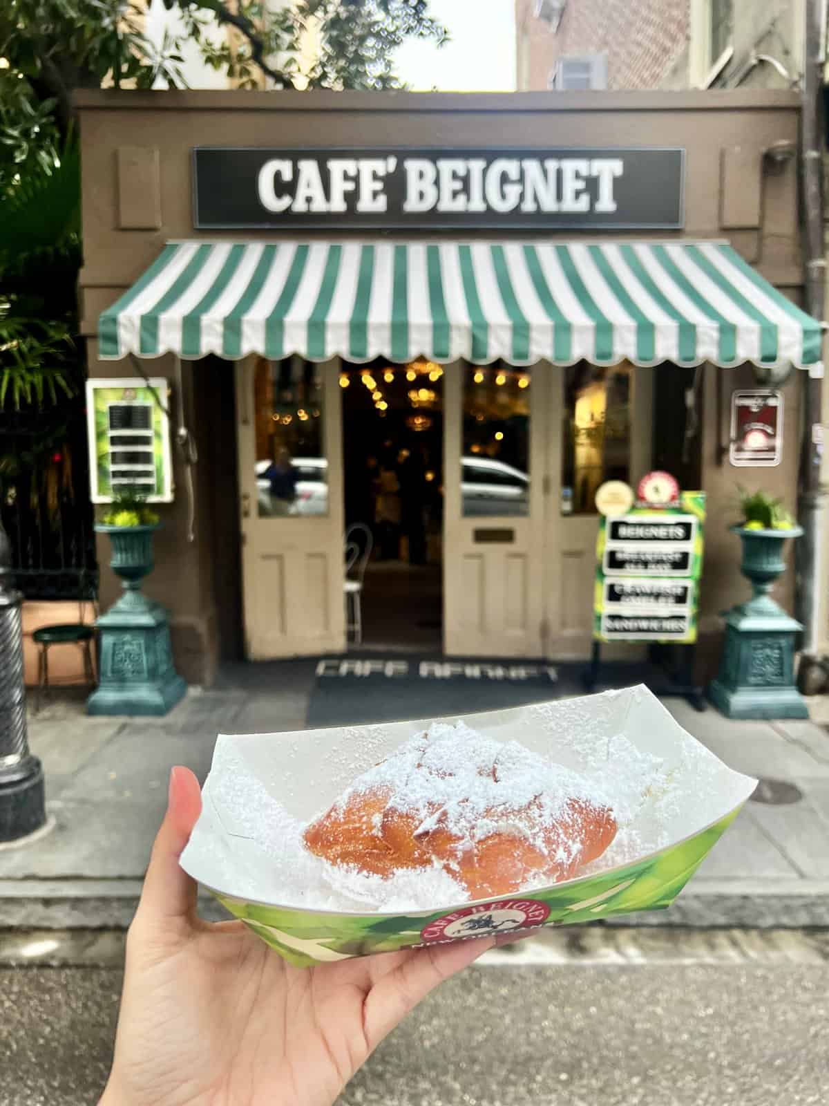 a hand holding a pastry in front of a restaurant